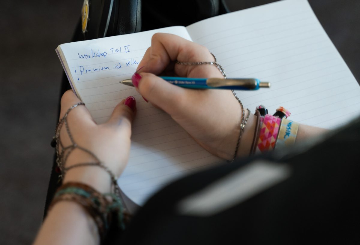 Zwei Hände einer Person, die sich Notizen in ein Notizbuch macht.