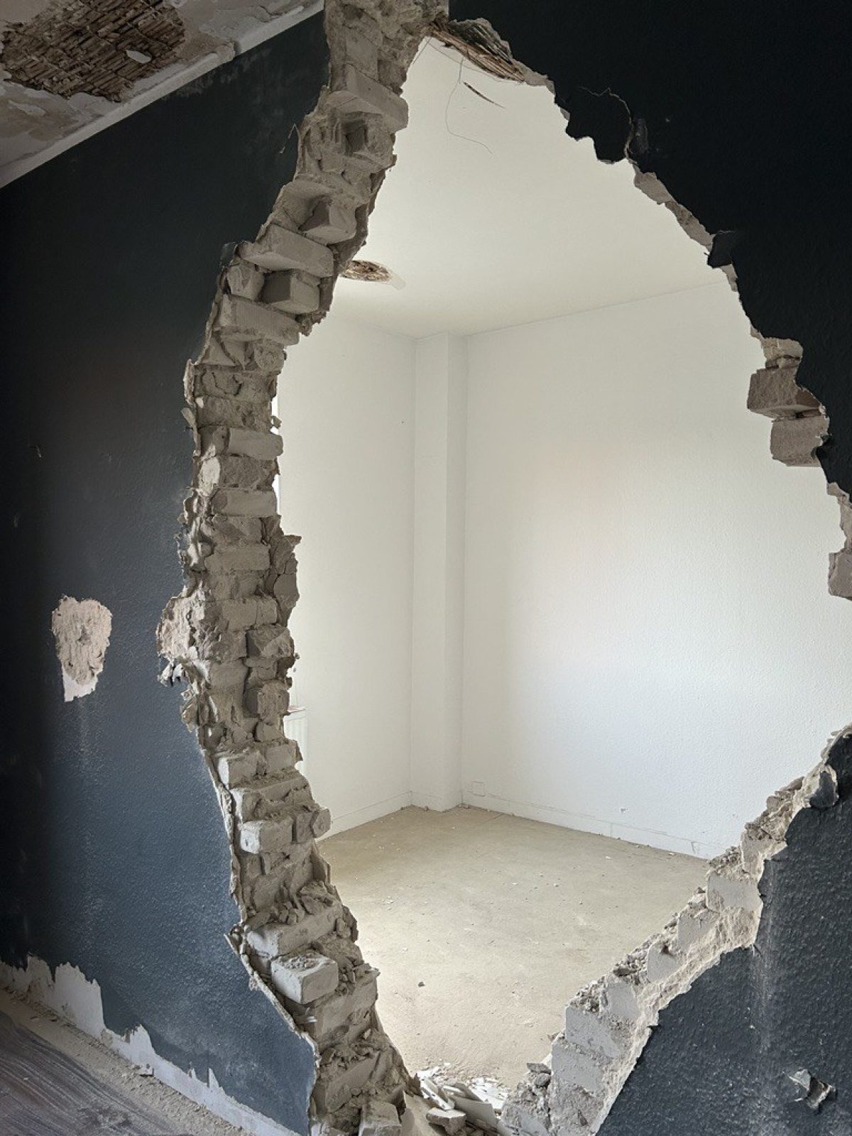 Auf dem Bild ist die Innenwand eines Hauses zu sehen, in die ein großes Loch geschlagen wurde, um zwei getrennte Räume zu einem großen Raum zu machen.