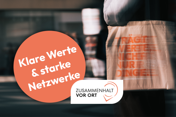 Teilweise unscharfe Aufnahme einer Person mit einem hellen Jutebeutel, auf dem orangefarbener Text in Großbuchstaben steht. Darauf einer ein rundes, orangefarbenes Textfeld mit "Klare Werte & starke Netzwerke" und ein Logo von Zusammenhalt vor Ort.