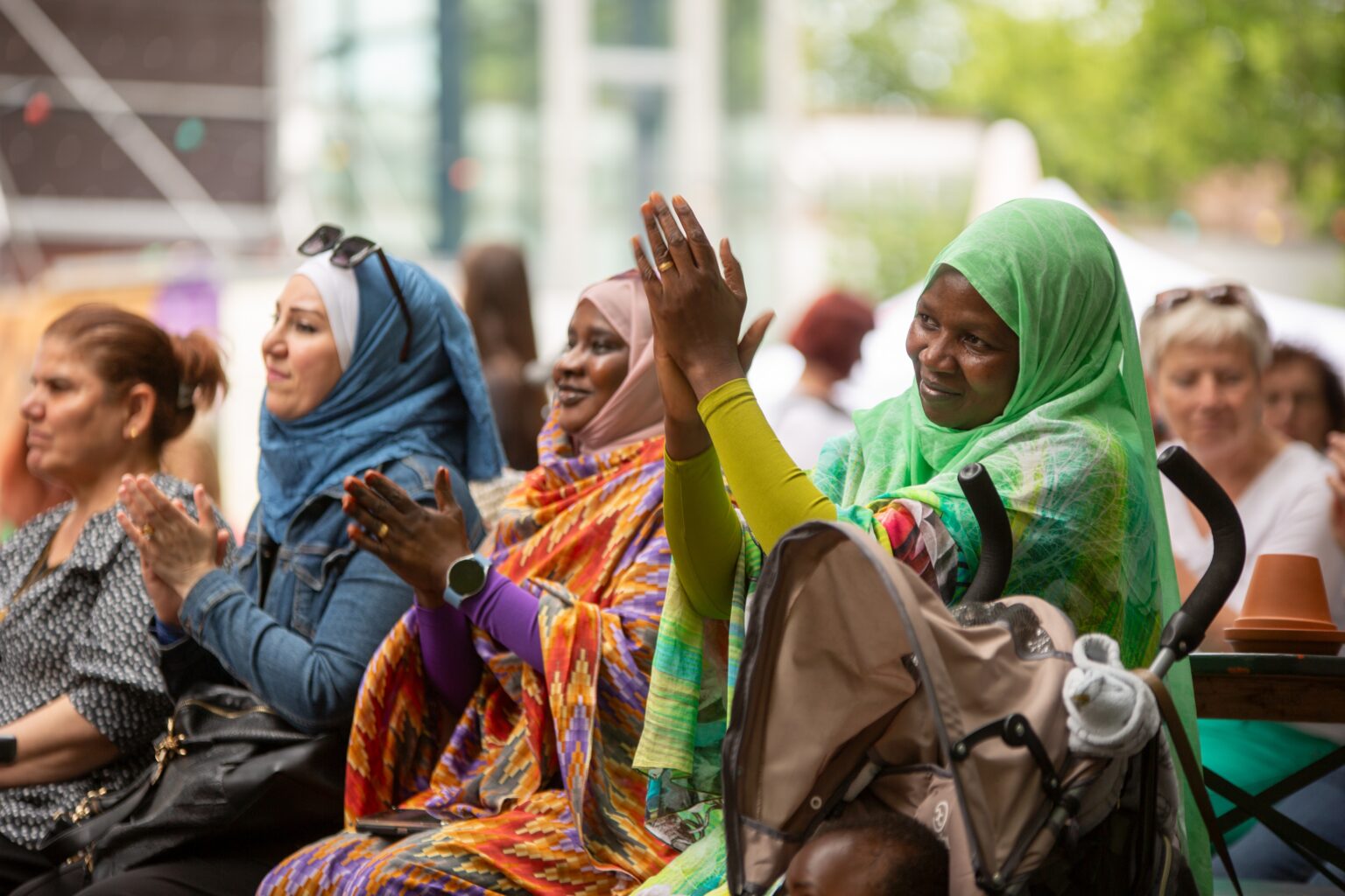 Mehrere Frauen sitzen im Publikum und applaudieren. Im Vordergrund steht ein Kinderwagen.