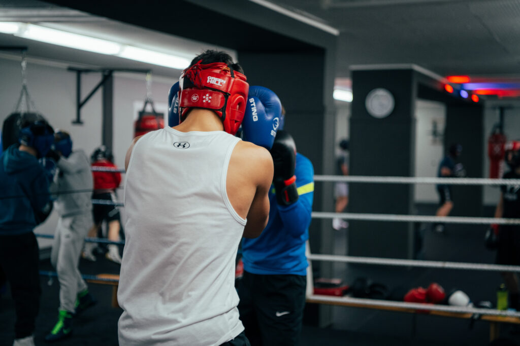 Zwei Boxer mit Kopfschutz beim Training in einem Boxstudio.