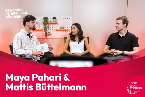 Maya Pahari und Mattis Büttelmann im Gespräch mit einem Moderator im Studio. Ihre Namen stehen auf einer roten Fläche im unteren Bildbereich.